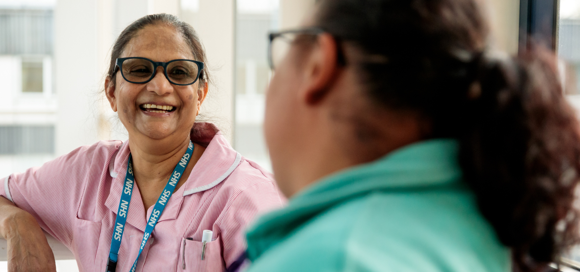 Woman smiling wearing a Barts Health NHS staff lanyard.